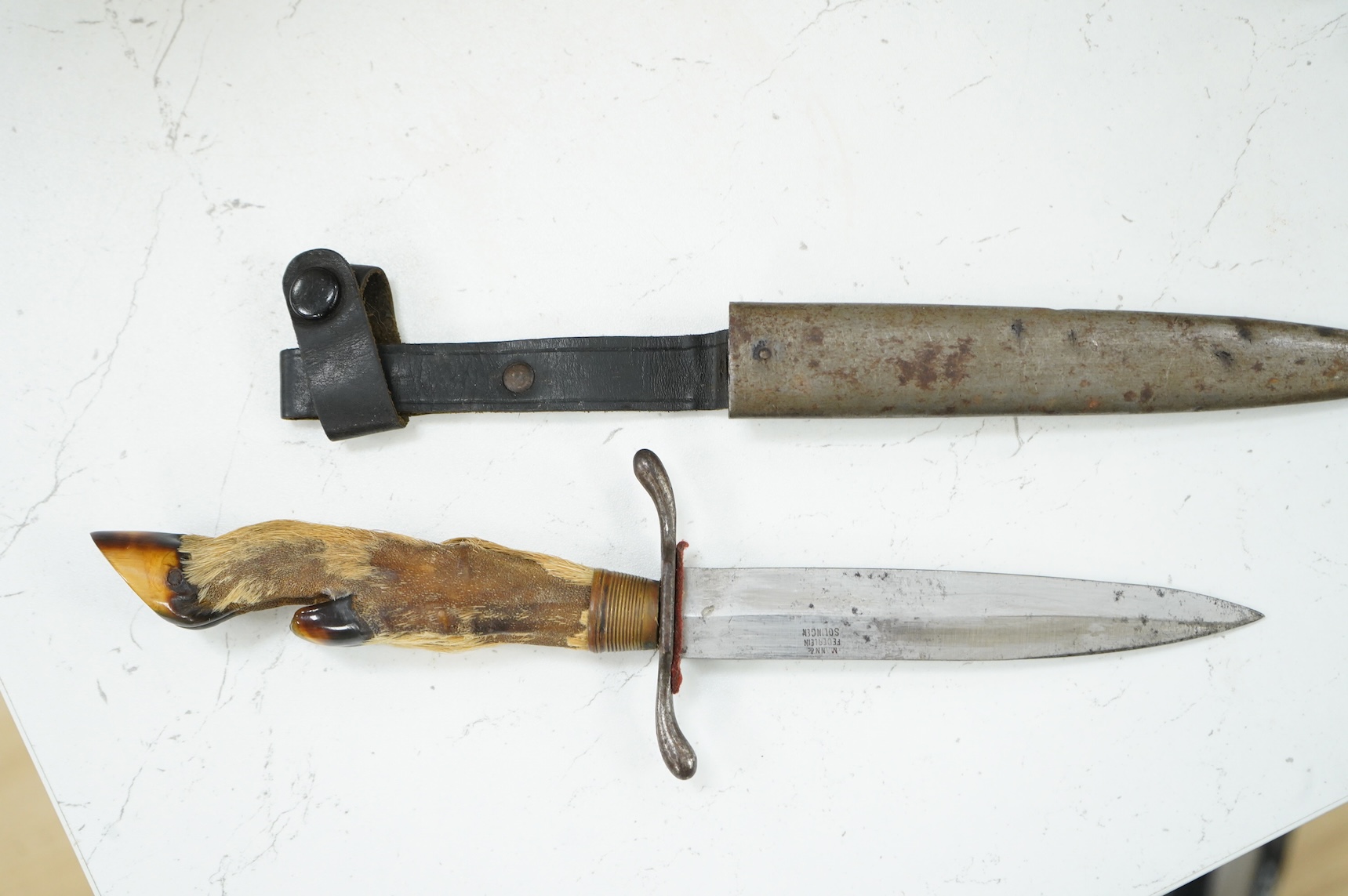 A First World War German Deer Hoof Fighting Knife, with a deer’s hoof grip, brass ferrell and steel cross guard, in original steel scabbard with leather belt loop mount, single edged blade with makers mark to one side; M